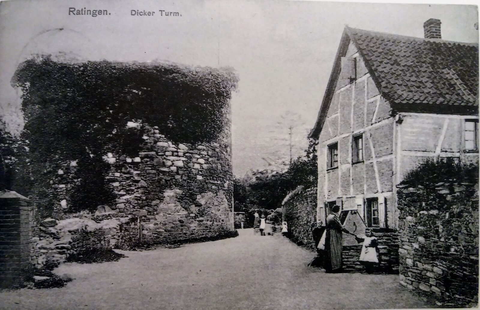 Historische Ansichtskarte von Ratingen mit dem Dicken Turm, einem alten Fachwerkhaus und Personen, die gemütlich auf einem Weg spazieren gehen.