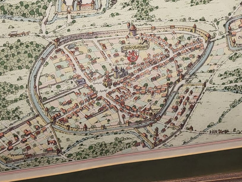 Eine liebevoll gezeichnete historische Stadtansicht von Ratingen mit Stadtmauer, Türmen, Kirche und Marktplatz in einer charmanten, alten Kartenoptik.
