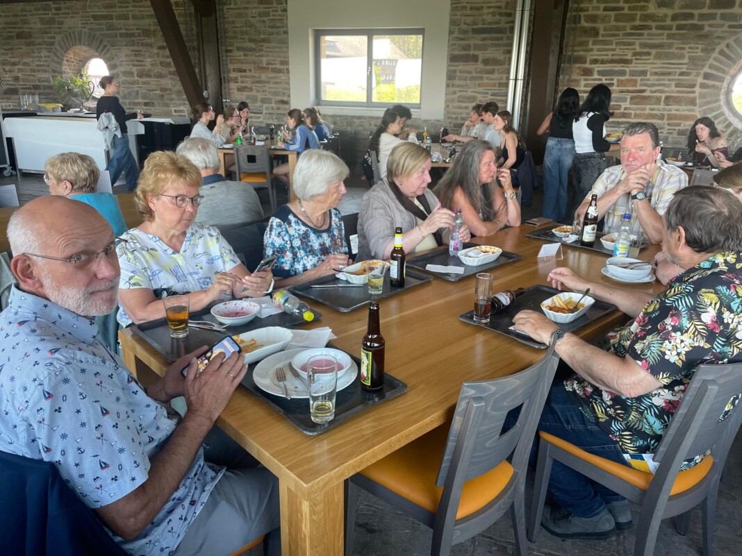 Eine fröhliche Gruppe von Menschen sitzt in einem rustikalen Raum mit Steinwänden an einem langen Holztisch und genießt gemeinsam eine Mahlzeit.