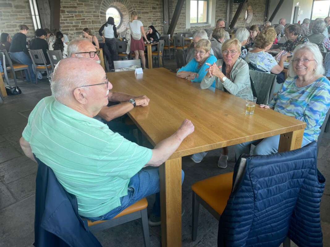 Eine fröhliche Gruppe älterer Menschen sitzt in einem gemütlichen Raum mit Steinwänden an einem großen Holztisch und unterhält sich angeregt.