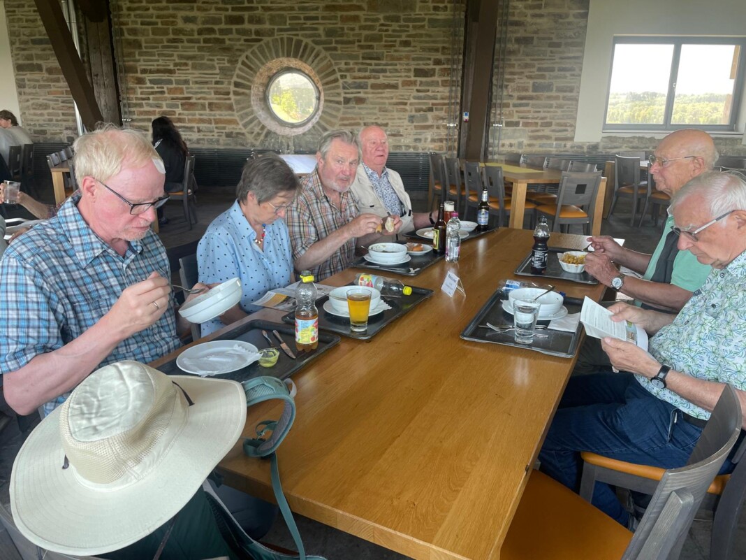 Eine fröhliche Gruppe älterer Menschen sitzt gemeinsam an einem langen Holztisch in einem rustikalen Raum und genießt eine entspannte Mahlzeit.