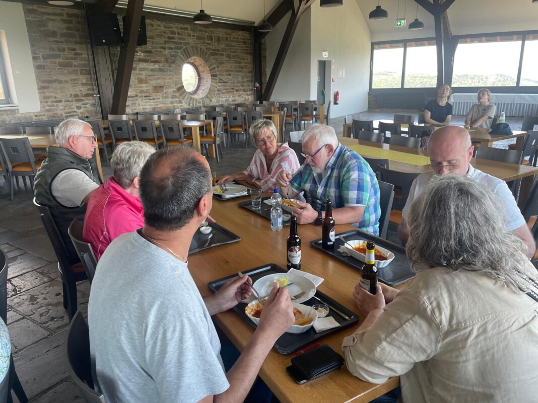 Eine fröhliche Gruppe von Freunden sitzt in einem gemütlichen Raum mit Steinwand an einem langen Holztisch und genießt gemeinsam ein Mittagessen.